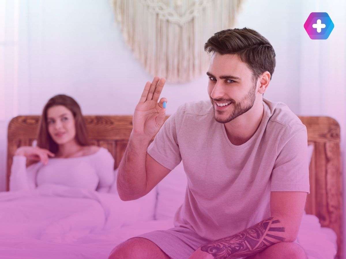 man smiling holding viagra tablet with woman in bed behind him